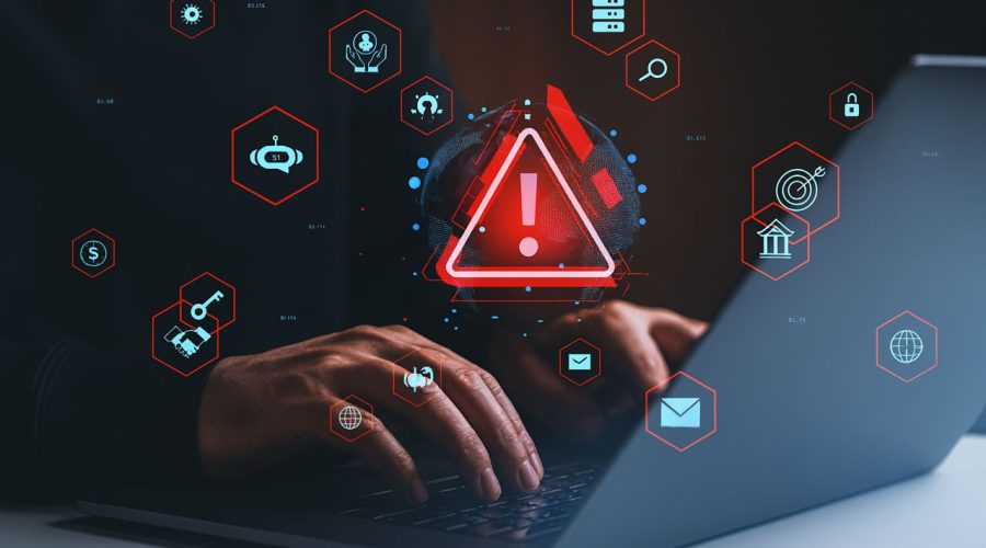 Hands typing on laptop with glowing red warning icon and security symbols floating around — 24/7 threat monitoring and rapid incident response for Minnesota businesses